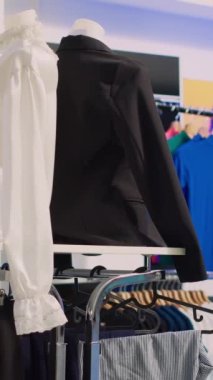 Dikey video: Moda terziliğiyle dolu alışveriş merkezi butiği, şık resmi kıyafetlerle dolu raflar. Askıda şık gömlekleri olan boş elbise galerisi, küçük işletme konsepti..