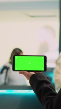 Dikey video: Asyalı asistan telefonda izole edilmiş yeşil ekran gösteriyor, krom anahtar şablonlu akıllı telefon görüntüsü kullanıyor. Kadın çalışan tutma aygıtı boş model ve kopyalama alanı, giyim mağazası