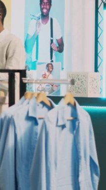 Dikey video: Genç bir kadın kasada ürünlere para ödüyor, moda kıyafetler almadan önce mağaza çalışanıyla konuşuyor. Kadın müşteri alışveriş merkezindeki pos terminalinde işlem yapıyor.