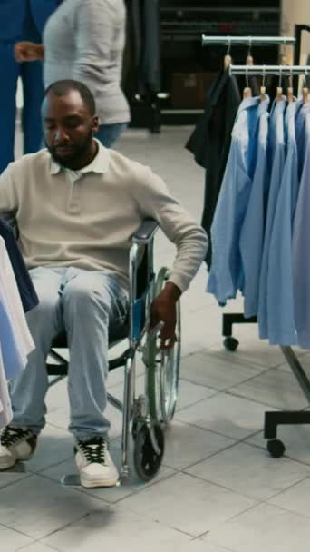 Вертикальное Видео Молодой Взрослый Инвалид Колясочник Покупает Современную Одежду Магазине — стоковое видео