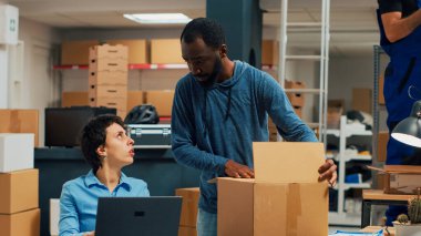 African american man signing delivery papers and shipping goods, working on packing warehouse merchandise. Small business owners doing product management with logistics. Handheld shot.