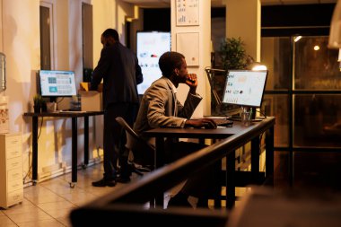 Yönetici yönetici bilgisayar pazarlama raporunu analiz ediyor, şirket stratejisinde fazla mesai yaparken mali grafikleri kontrol ediyor. Afrikalı Amerikalı iş adamı yatırım planı