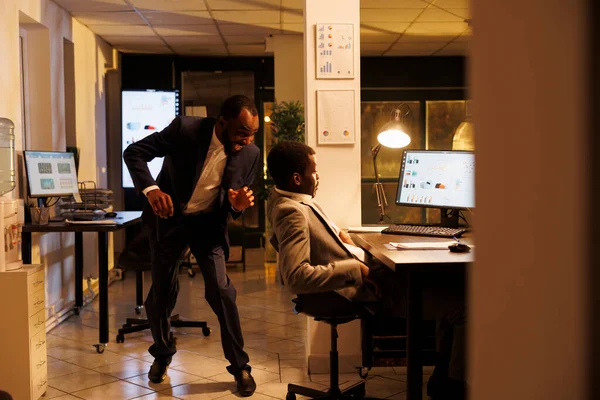 Funny manager scares his sleepy colleague in startup office, worker falling asleep on desk in startup office. African american employees working late at night at marketing strategy