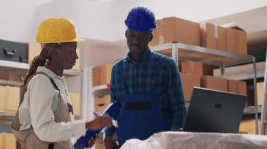 Depoda kalite kontrol yapan kadın denetçi, depo raflarından stok ürünleriyle çalışıyor. Çalışanlardan oluşan bir ekip teslimat için malları kontrol ediyor. El kamerasıyla..