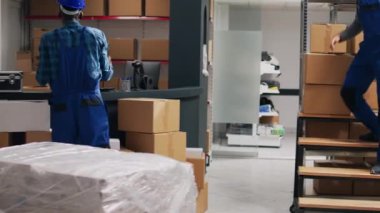 Afro-amerikan denetçi paketler içinde mallara bakıyor, çeşitli çalışanlarla ürün göndermek için çalışıyor. Tulumlu genç bayan yönetici lojistik ürünleri kontrol ediyor..