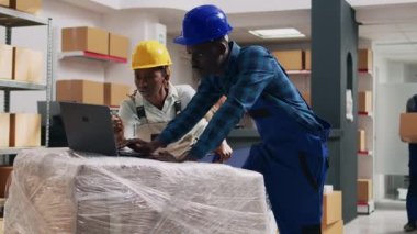 Dizüstü bilgisayarda mal dağıtımı yapmayı planlayan işçiler. Depoda eşyalar ve karton paketlerde ürünlerle çalışıyorlar. Genç çalışanlar bilgisayar ve imalat işlerinde envanter çıkarıyorlar..