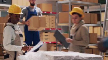 Depo çalışanlarından oluşan bir ekip depo alanındaki teslimat sevkiyatından bahsediyor, paketlerdeki mallara bakıyor. Çeşitli kadınlar depoda mal ve ürünleri kontrol ediyor. Üçayak atışı.