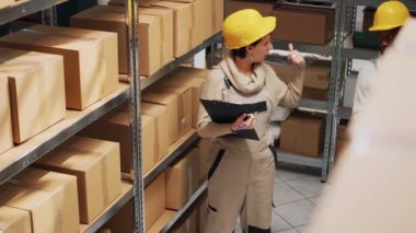 Depo çalışanı depodaki kargo paketlerini analiz ediyor. Dağıtıma mal göndermek için stok envanteri üzerinde çalışıyor. Karton kutuları kontrol eden kadın, endüstriyel stoklar..