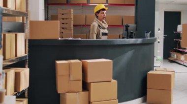 Depo müdürü depoda barkodlu malları kontrol ediyor. Endüstriyel iş için stok mallarına bakıyor. Ürün paketleri ve tablet üzerinde tarayıcı kullanan genç denetçi.