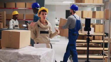 Depoda reklam videosu çeken genç bir yetişkin, çevrimiçi sosyal medya sayfasında ürünlerin kutularını gösteriyor. Depo çalışanları halkla ilişkiler ve endüstriyel ürünleri kaydetmek için cep telefonu kullanıyor..