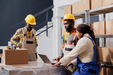 Afro-amerikan paket taşıyıcıları dizüstü bilgisayarda paket paketleme ve sipariş listesini kontrol ediyorlar. Tüm siyah erkek ve kadın depo işçileri depo odasındaki elektronik pena biletine bakıyor.