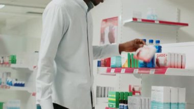 Genç adam eczane raflarından ilaç kutusu alıyor, tedavi için ilaç ürünlerine bakıyor. Müşteri takviye paketleri ve eczane malzemeleri kontrol ediyor. El kamerasıyla..