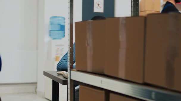 年轻的男性员工在纸板箱里检查产品 在储藏室里查看笔记本电脑上的库存 小企业主使用仓库货架和货架上的商品 — 图库视频影像