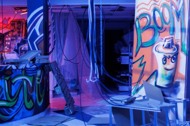 Terk edilmiş eski depodaki floresan lambaların altında parlayan duvarlara sprey boya. Ürkütücü ve kirli görünüyor. Parlak neon ışıkları olan boş harabe bina, yok edilmiş alan.