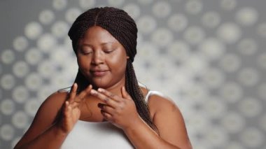 Afrikalı Amerikalı kız stüdyoda nemlendirici kremi tanıtıyor, cilt bakımı kampanyası için serum ve yüz kremi sürüyor. Dermatoloji kozmetik ürünleri kullanan kusursuz doğal model..