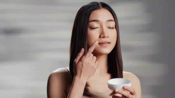 Modelo Asiático Que Aplica Crema Facial Antienvejecimiento Las Mejillas Promoviendo — Vídeo de stock