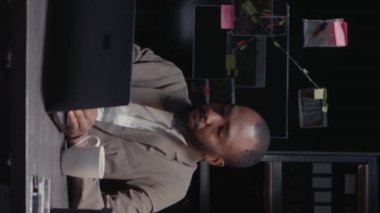 Dikey video: Afrikalı Amerikalılar polis arşivindeki dava kayıtlarını inceliyor, adli kanıtlarla birlikte dedektif panosuna bakıyorlar. Olay odasındaki suç bilgilerini inceleyen özel müfettişler..