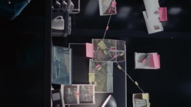 Dikey video: Kadın dedektif kanıt panosunda ipuçları buluyor, arşiv odasında suç çözme üzerinde çalışıyor. Kadın araştırmacı güvenlik kamerası görüntülerini inceliyor, içgörü ve ayrıntıları arıyor..