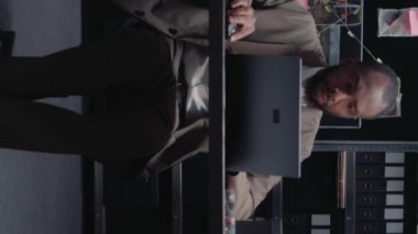 Dikey video: Erkek ajan kanıt odasında dava bilgileriyle çalışıyor, yeni ipuçları bulmak için gözetim fotoğraflarını inceliyor. Polis memuru araştırma için geçmişini araştırıyor. El kamerasıyla..
