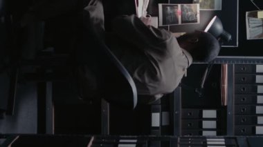 Dikey video: Güvenlik kamerası görüntülerini inceleyen iki polis memuru, soruşturma için arşiv odasında dava dosyaları üzerinde çalışıyor. Dedektiflik haritasındaki fiziksel kanıtları inceleyen müfettişler,