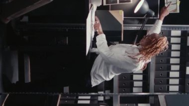 Dikey video: Afro-Amerikan ajanları ofiste dava raporlarını analiz ediyor, cezai soruşturma üzerinde çalışıyorlar. Polis arşivindeki tanık ifadelerini okuyan müfettişler dedektif haritasına bakıyor..