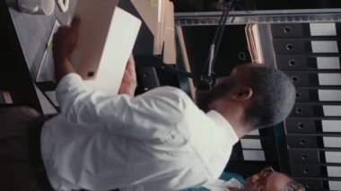 Dikey video: İki polis memuru arşiv odasındaki güvenlik kamerası görüntülerinden bahsediyor, detayları ortaya çıkarmak için suç davasını inceliyorlar. Dedektifler dedektiflik yapıyor, soruşturma yürütüyor.