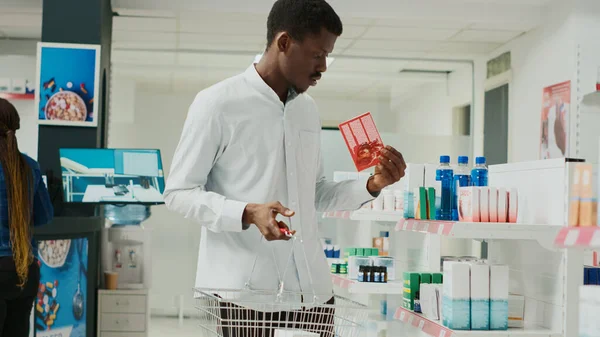 Male customer taking vitamins box from drugstore shelves, looking at pharmaceutical products to buy medicine. Young adult checking supplements boxes and medical supplies. Handheld shot.