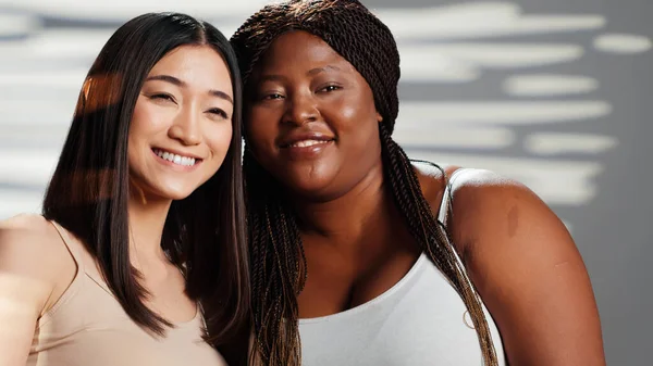 Interracial girls embracing and expressing self confidence, doing skincare and advertisement in studio. Happy women posing and showing self acceptance, body positivity femininity concept.