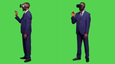 Kamerada video kulaklık kullanan bir şirket çalışanı. Sanal gerçeklik gözlükleri ve stüdyoda 3 boyutlu simülasyonla çalışıyor. Modern cihazlı genç girişimci tüm vücudu yeşil ekranda.