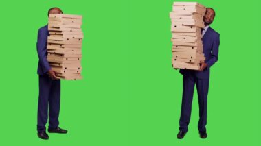 Erkek girişimci büyük pizza kutularını kameraya çekiyor, tüm vücudunun üzerinde fast food siparişi taşıyor. Takım elbiseli genç adam stüdyoda yemek yiyor..