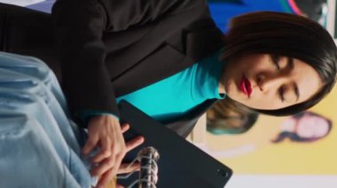 Dikey video: Mağaza yöneticisi tabletli butik stok üzerinde çalışıyor, askılardaki ve raflardaki tüm kıyafetleri analiz ediyor. Kadın çalışan, giyim mağazasında envanter yapıyor, ürünleri inceliyor. El kamerasıyla.