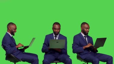 Stüdyoda dizüstü bilgisayarda çalışan, kablosuz bilgisayarlı bir koltukta oturan Afrikalı Amerikalı bir yönetici. Ofis çalışanının takım elbisesi yeşil ekranın üzerinde taşınabilir bilgisayar kullanıyor..
