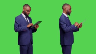 Ofis müdürünün elinde stüdyoda çalışması için dijital bir cihaz var. Sosyal medya uygulaması üzerinden Greescreen arka planında geziniyor. Modern tablet kullanan resmi takım elbiseli şirket çalışanı, çevrimiçi ağ.