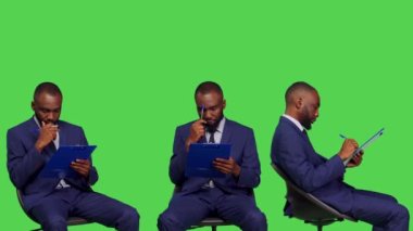 Sandalyedeki erkek girişimci iş bilgileri yazıyor, beyin fırtınası yapıyor ve dosyalar hakkında notlar alıyor. Şirket yöneticisi resmi takım elbise giyiyor ve pano kağıtlarını yeşil ekran üzerinde tutuyor..