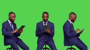 Girişim yöneticisi dijital aygıtla internette geziniyor, yeşil ekran arkaplanının üzerinde oturuyor. Profesyonel işadamı internet ağında kaydırma yapmak için tablet kullanıyor, resmi kıyafet.