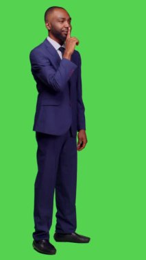 Dikey video: Afro-Amerikan işçilerin sessiz hareketlerini, sır saklamalarını ve gizli kalmalarını gösteren yan görüş. Stüdyoda gizlilik ve sessizlik işareti gösteren özel girişimci, kendinden emin.