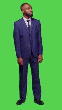 Dikey video: Kol saatini kontrol eden ve stüdyoda bekleyen genç bir yetişkinin iş yerinde çalışmadan önce saate baktığı ön görüntü. Takım elbiseli girişimci özgüvenle poz veriyor