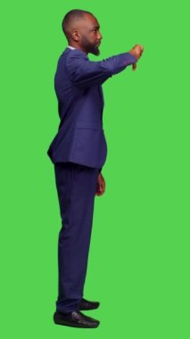 Dikey video: Negatif ofis çalışanının profili stüdyoda baş parmak işi yapıyor, yeşil ekran arka planda resmi takım elbise giyiyor. Genç işadamı, hoş olmayan davranışlar sergiliyor ve bunu onaylamıyor.