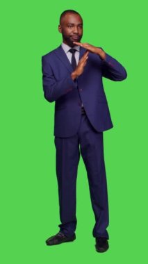 Dikey video: Şirket çalışanının tüm yeşil ekran üzerinde duraklama hareketi yaparken ön görüntüsü. Reddetme ve reddetme sembolü gösteren genç işadamı, giriş yap