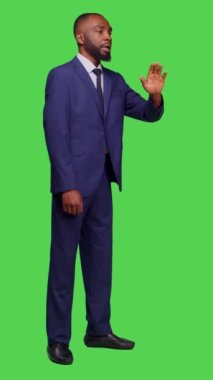 Dikey video: Girişimci işçilerin insanlarla konuştuğu ve stüdyoda el salladığı, iş elbisesini tüm yeşil ekranda giydiği yan görüntü. Genç işadamı kamerada sohbet ediyor, birini arıyor.