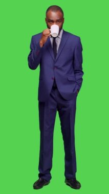 Dikey video: Erkek yöneticinin kamerada kahve içerken ön görüntüsü, tam yeşil ekranda kafein içeceği servis ediyor. Kurumsal işçiler sıcak içeceklerin tadını çıkarıyorlar, iş giyiyorlar.