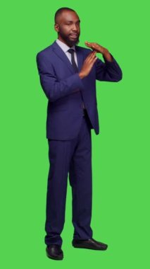 Dikey video: Şirket çalışanının tüm yeşil ekran üzerinde duraklama hareketi yaparken yan görünümü. Reddetme ve reddetme sembolü gösteren genç işadamı, giriş yap