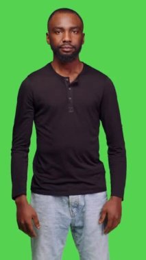 Dikey video: Genç erkek modelin görüntüsü kamera önünde şık poz veriyor, yeşil ekran arkaplanının üzerinde duruyor. Kot pantolon ve gömlek giyen, kendine güveni olan, pozitif yüz ifadesi olan sıradan biri.
