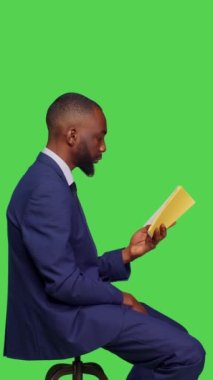 Dikey video: Stüdyoda edebiyat kitabı okuyan, ofis elbisesi giyen modern girişimci profili. Olumlu iyimser adam yeşil ekranda ders veriyor.