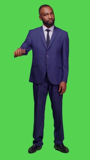 垂直ビデオ 負のオフィスワーカーのフロントビューは スタジオで親指を行う 緑の画面の背景に正式なスーツを着て 若いビジネスマンはジェスチャーを嫌い 不承認を表明する — ストック動画