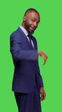 Dikey video: Takım elbiseli bir şirket yöneticisinin birini buraya çağırıp yeşil ekran arkaplanının üzerinde durmaya çağırması. Genç adam iş adamı olarak çalışıyor.