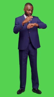 Dikey video: Saati kontrol etmek için kol saatine bakan şirket çalışanlarının ön görüntüsü, tam vücut yeşil ekran arkaplanı üzerinde dakik olmak. Ofis kıyafetli genç girişimci kontrol saati ve çalışma saati