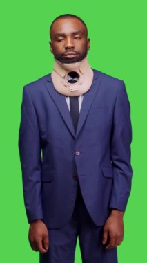 Dikey video: Yaralı erkek modelin ağrıyı hafifletmek için boyun korsesi kullanması, stüdyoda tıbbi nedenlerden ötürü omurga kırığı oluşması. Takım elbiseli genç işadamı yaka köpüğü giyiyor.