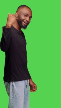 Dikey video: Afro-amerikalı birinin sembolize edişinin yan görüntüsü, birinin ona katılmasını ve eşlik etmesini istemesi. Kot pantolonlu ve gömlekli genç bir yetişkin yeşilin üzerinde dikilen bir insanı arıyor.