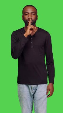 Dikey video: Özel kişinin sessiz kalma hareketini parmak ile göstermesi, mahremiyeti ifade etmesi ve gizli kalması. Genç yetişkin, yeşil ışıkta sessiz sessizlik işareti yapıyor.